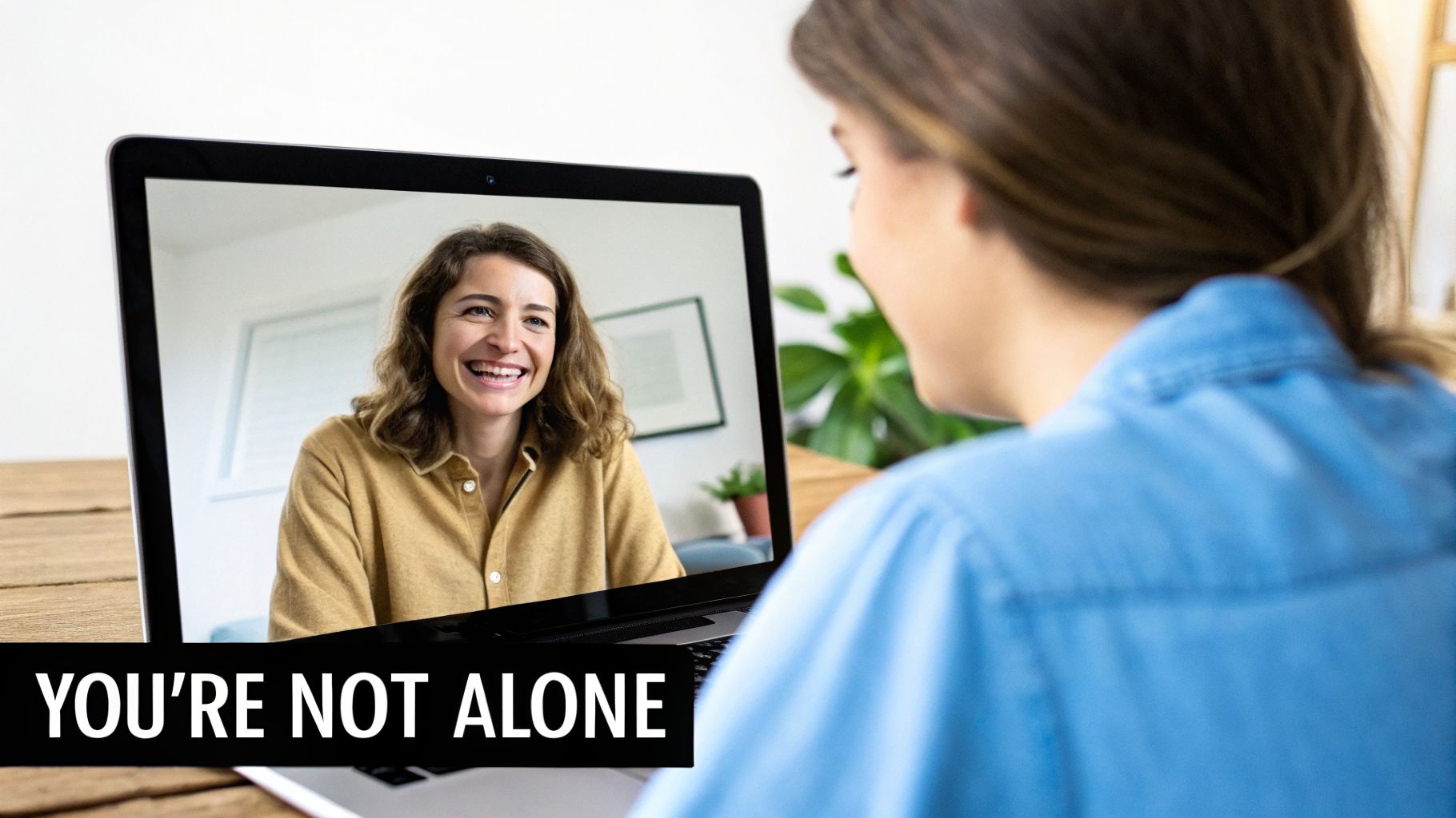 Two women on a video call, one smiling on the laptop screen, the other watching, with the text 'YOU'RE NOT ALONE'.