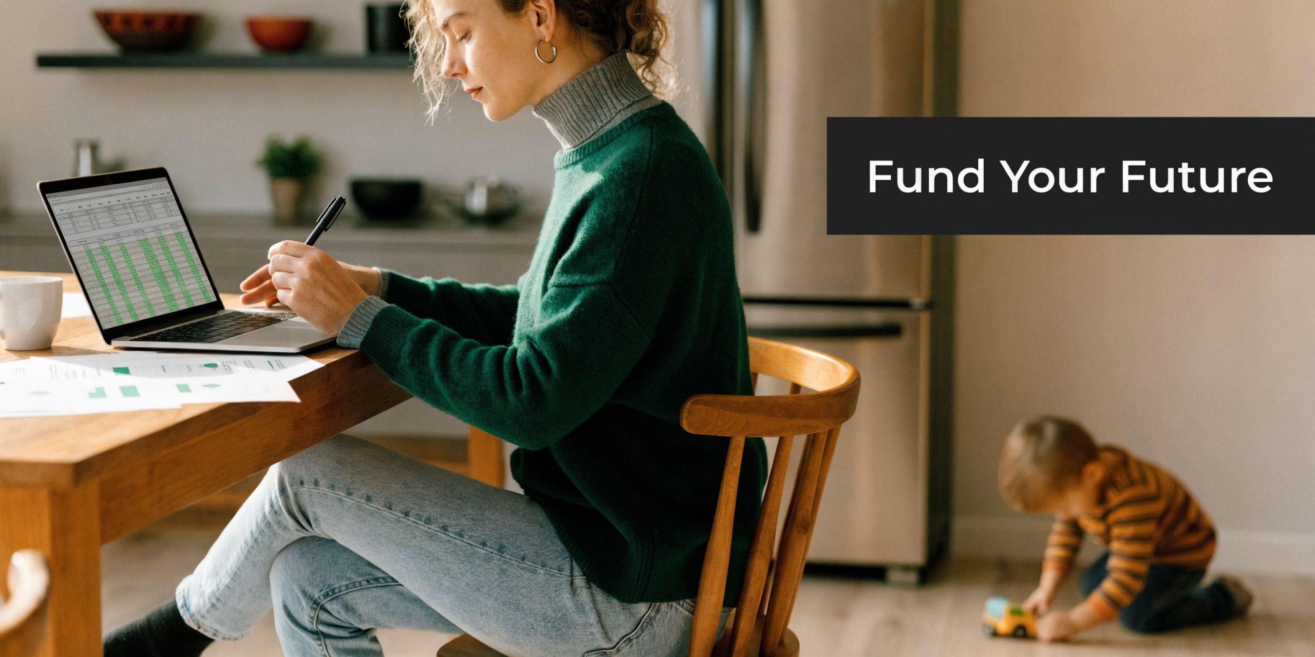 A focused woman reviewing financial spreadsheets on a laptop at a kitchen table while her toddler plays nearby.