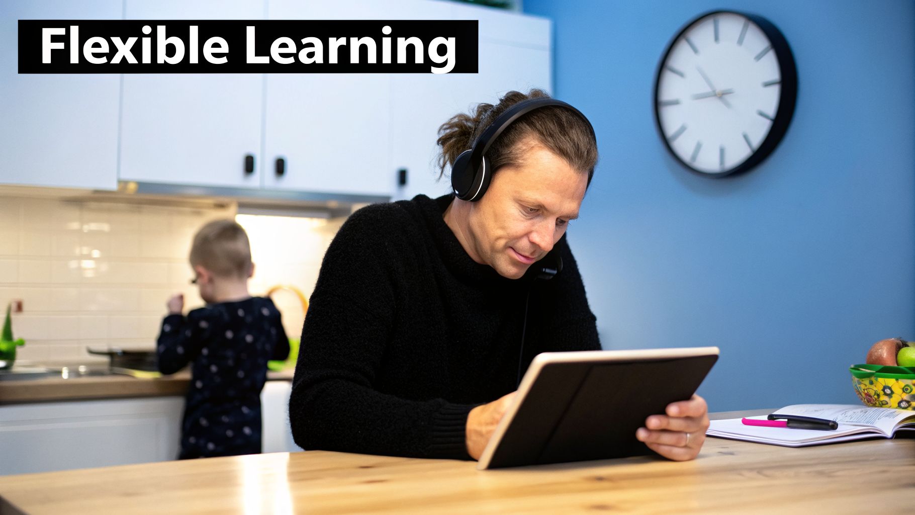 A man wearing headphones with a mic uses a tablet for online learning at a wooden desk.