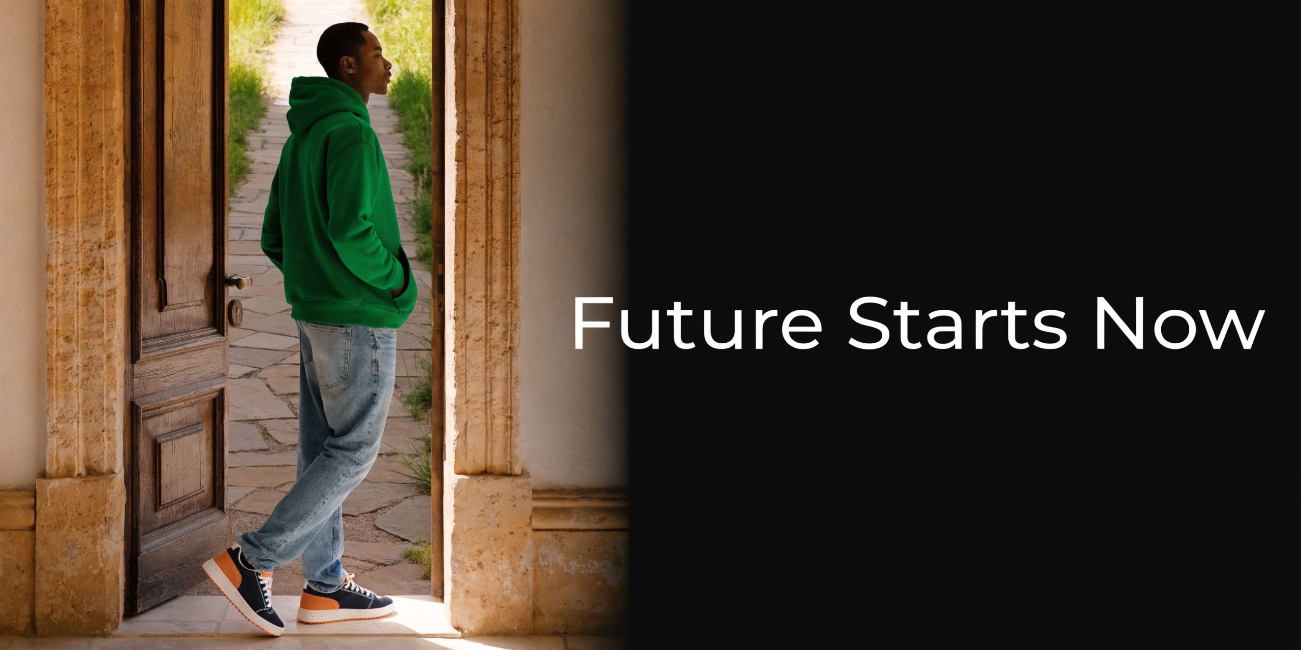 A young man standing in a doorway wearing a green hoodie, jeans, and colorful casual sneakers.