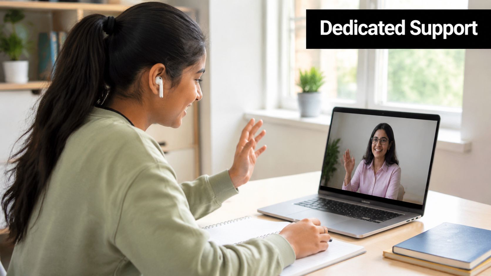 A student attending an online A Level economics session on a laptop while waving to her teacher.