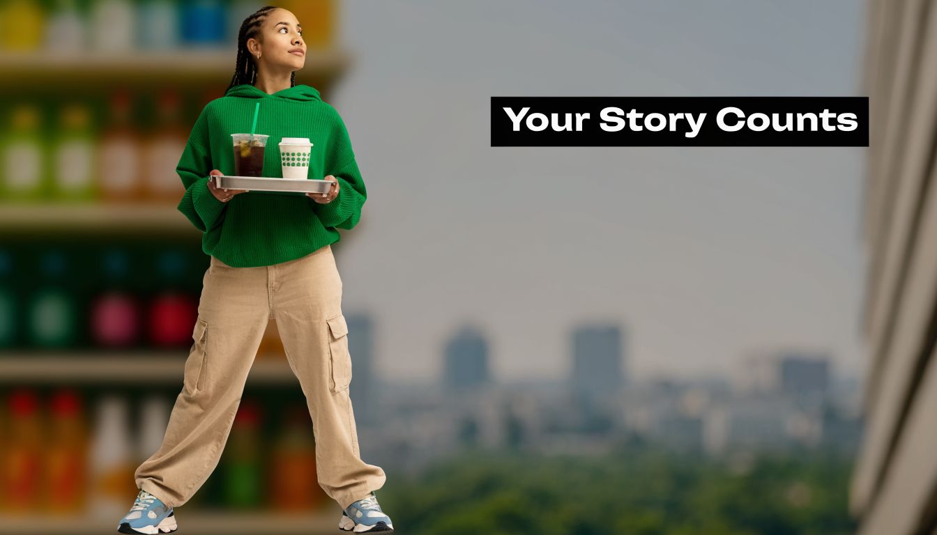 A young woman in a green hoodie holding a tray of drinks standing against a blurred background.