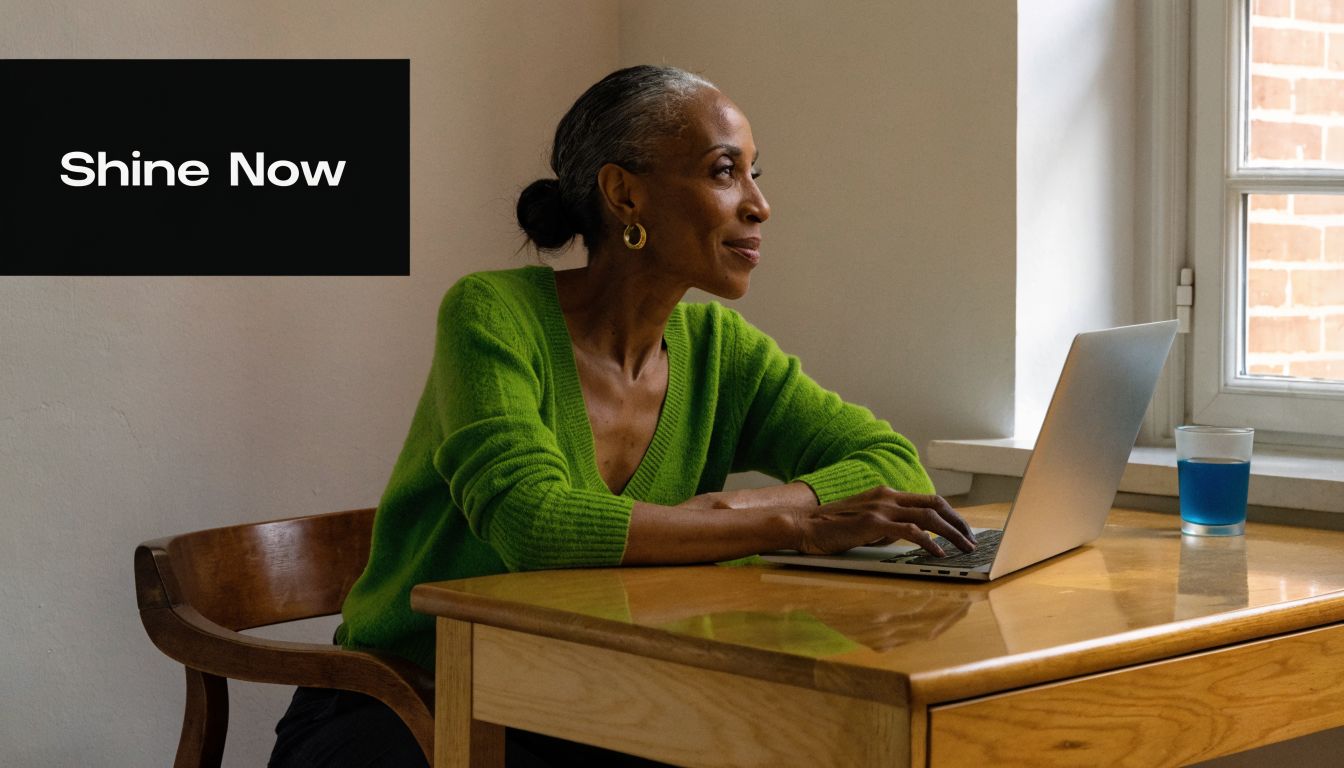 A professional woman in a bright green sweater working on her laptop by a sunlit home window.
