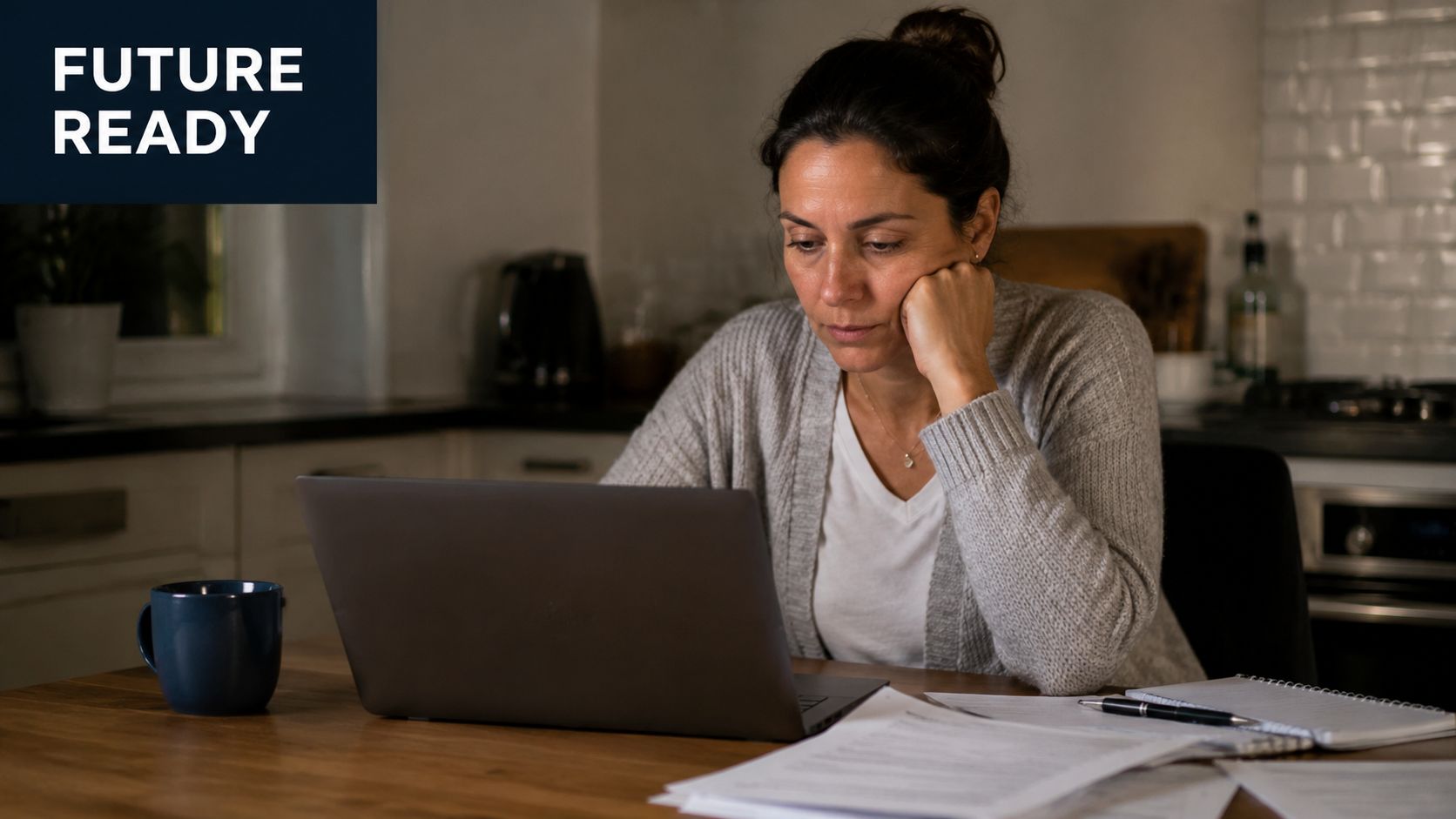 A woman looks focused while sitting at a kitchen table working on her laptop with papers nearby.