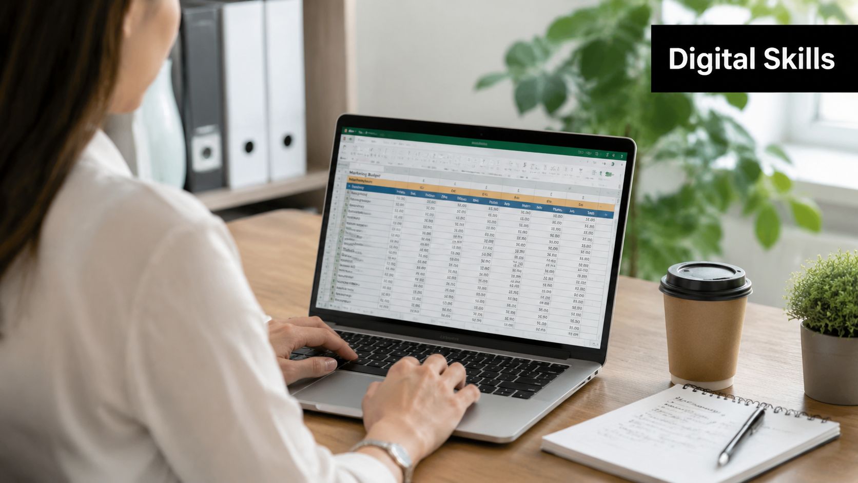 A woman working on a marketing budget spreadsheet on her laptop at a wooden office desk.
